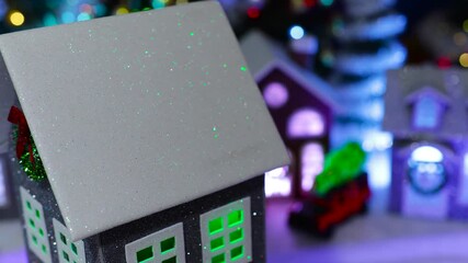 A close-up of a grey house rotating in front of a decorated Christmas village