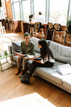Fototapeta Two female office workers smiling and sitting on a couch while holding documents and a notebook