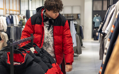 Teenage boy in red puffer jacket shopping for clothes in fashion store — youth style, generation Z fashion, modern retail, winter outfit, consumer behavior, teen lifestyle © Светлана Мищенко