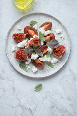 Plate with fig fruit, cottage cheese and tomato salad, vertical shot on a white stone background, elevated view