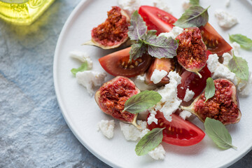 Salad with tomato wedges, fresh torn figs and cottage cheese served on a white plate, horizontal shot, close-up