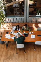 A female employee looks at a document being shown to a male and female employee sitting next to her at a table