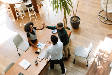 A female employee laughs and gives a high five to a male employee who is standing at the desk...