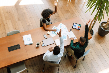 A group of three workers raised their hands while sitting at a table