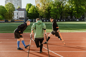 A group of three men are stretching their legs and two of them are leaning on the ground with crutches