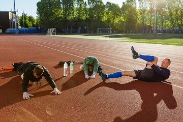 A group of three men stretching and warming up on a running track