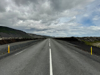 straight empty icelandic road through lava fields continuing to the horizon with a dramatic cloudscape above