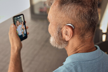 Senior man with hearing aid behind the ear communicates with his family via video communication via...