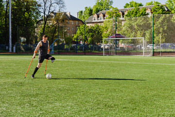 A man looks at a ball in front of him on a field while holding crutches