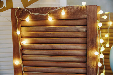 Warm-toned string lights with globe bulbs draped over a rustic wooden slatted screen, creating a cozy and festive atmosphere for a celebration