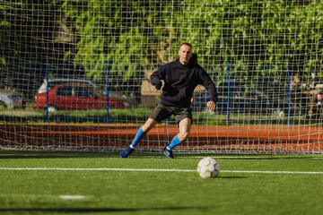 A male goalkeeper runs to the side and looks at the ball on the field in front of him