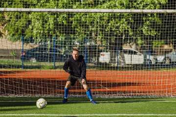 A male goalkeeper stands at the goal and is about to catch the ball in front of him