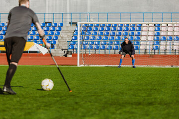 A man stands in front of a goal and looks at a man on crutches standing near a ball
