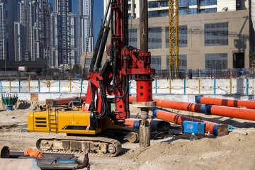 A heavy-duty piling machine operating at a modern urban construction site, surrounded by high-rise buildings and infrastructure materials. Used for deep foundation drilling in large-scale commercial o