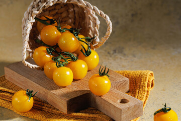 Fresh yellow cherry tomatoes on wooden cutting board with rustic towel and natural background