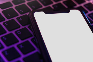 Mock up, smartphone with white blank screen lying on laptop keyboard in violet light, trendy digital concept for modern gadget, technology, or application design projects. Space for text