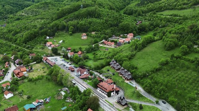 Aerial view of Mokra Gora railway station in Serbia, surrounded by green hills and traditional village houses in spring. Horizontal 4k footage