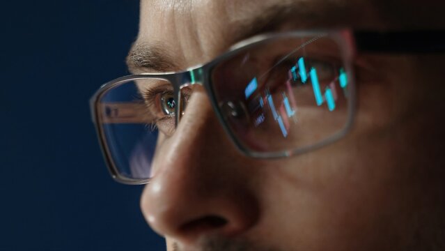 close up of professional trader closely monitors financial analytics, with forex and stock market charts reflected in his eyeglasses, assessing crypto market movements. 
