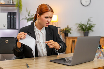 Young businesswoman at home office tears draft report after spotting error and decides fresh start immediately. Freelancer girl at table opens new file typing fast very focused on clear accurate text