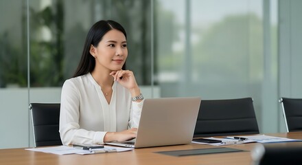 Thoughtful asian businesswoman working on laptop in modern office space