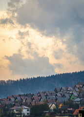Charming mountain townscape in Limanowa, Poland, with colorful houses nestled below forested hills under a glowing sunrise or sunset sky.