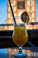 Yellow tropical cocktail with lime garnish on rooftop terrace overlooking historic Polish krakow city square at sunset, urban dining experience