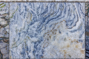 Close-up of aged and textured marble floor tiles featuring swirling blue and tan-toned veins on a white and light grey base, showing signs of wear and time.