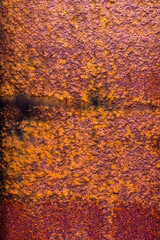 Metal surface with a thick layer of rust, exhibiting a predominantly purple hue with hints of orange and a rough texture