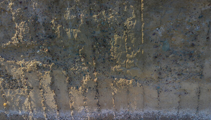 Rough, uneven concrete surface embedded with small pebbles and showing signs of age and wear under tangential harsh sun light showing all imperfections.