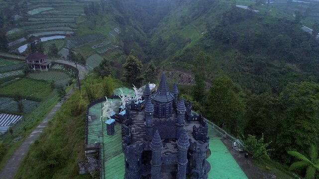 Aerial footage front view of Kahyangan black castle with green tropical landscape background
