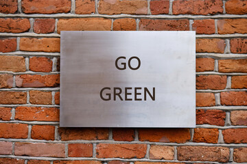 A metallic sign boldly stating the words GO GREEN hangs on a charming brick wall, encouraging everyone to adopt eco-friendly habits in a vibrant city atmosphere