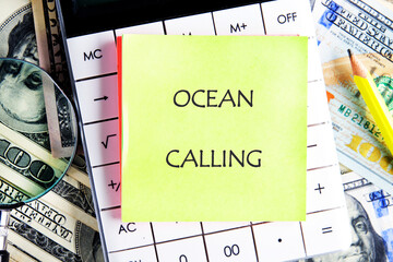 A bright sticky note reads ocean calling placed on a calculator surrounded by dollar bills and a...