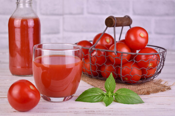 Tomato juice in a bottle and fresh tomatoes in a basket in the background.	