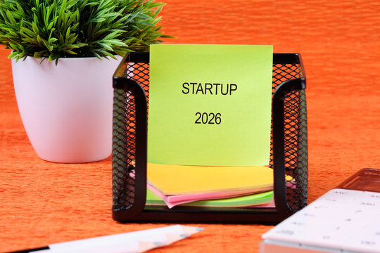Bright sticky notes in a black desk organizer show the project year 2026 for a startup. A green plant, calendar, and pen add to a productive workspace atmosphere
