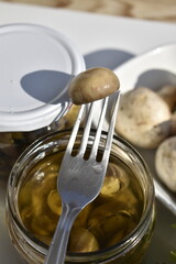 Marinated Mushroom Cap on a Fork with Fresh Mushrooms and a Jar of Pickled Mushrooms, Macro Photography