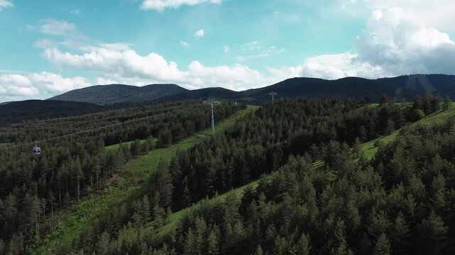 Aerial view of Zlatibor Grand Gondola cable cars moving across pine forests with Tornik mountain in the background on a spring day. Horizontal 4k footage