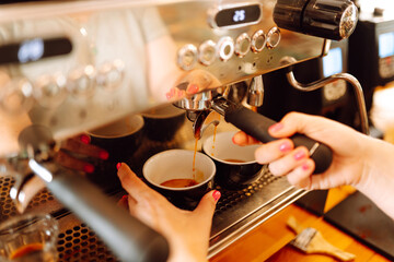 Experienced barista prepares freshly brewed coffee using professional coffee machine. In cozy coffee shop, espresso is poured from espresso machine into black cup. Small business, beverage concept.