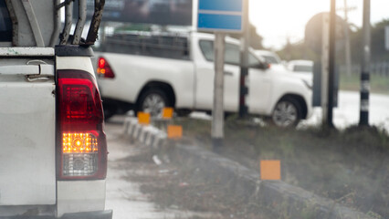 Naklejka premium Rear side on pickup car with turn on right signal for U-Turn on the road. Environment of traffic in the rainy time. on the road with drop of rainy. Water mist spreads across the floor.