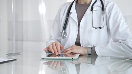 Physician in lab coat with stethoscope reviewing patient data on a tablet in a bright modern clinical office via touchscreen. Medicine and health care - Powered by Adobe