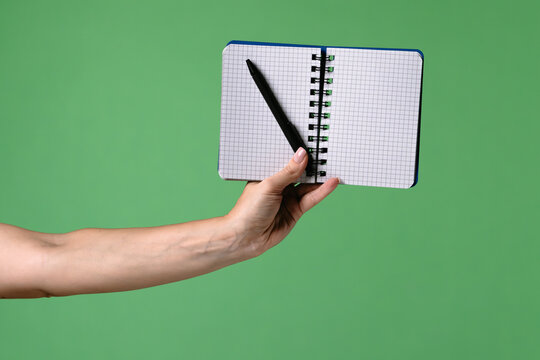 A woman hand holding an open notebook and pen on a green chroma key background. Shot for designs related to office, business, education and training.