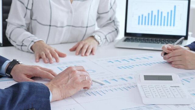 Business people professionals or accouters analyzing financial reports, charts and graphs on laptop and paper, using calculator to discuss strategy, budgeting and teamwork decisions