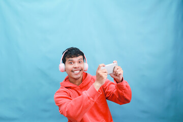 Naklejka premium Young man gaming with headphones and phone, smiling.