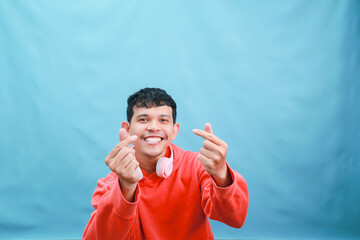 Happy Young Asian Man in Orange Hoodie Making Korean Heart Gesture.
