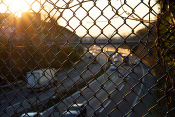 夕暮れの金網フェンス越しに見る高速道路の交通