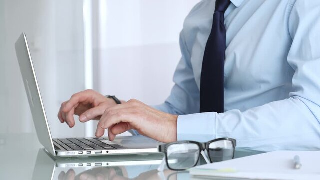 Businessman working on laptop in office, typing keyboard, focusing on professional corporate tasks. Business people concept