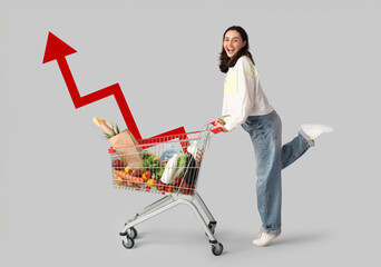 Beautiful young happy woman with full shopping cart on grey background