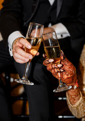 Close-up of the hands of bride and groom toasting with champagne glasses during wedding celebration. The bride’s hand is decorated with henna, creating a festive and romantic atmosphere
