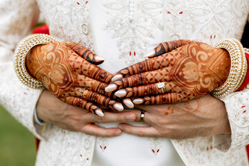 Close up of bride and groom embracing, showing beautiful mehndi on hands, wedding rings, and...