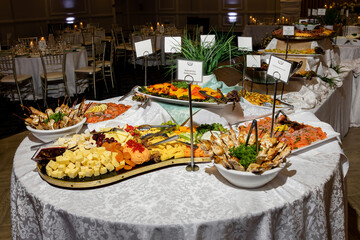 Elegant wedding buffet table with assorted gourmet appetizers, cheeses, grilled skewers, smoked salmon, and colorful vegetables, beautifully arranged in a banquet hall with candlelit tables
