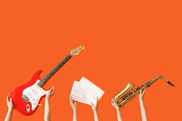 Female hands holding electric guitar, music notes and saxophone on red background